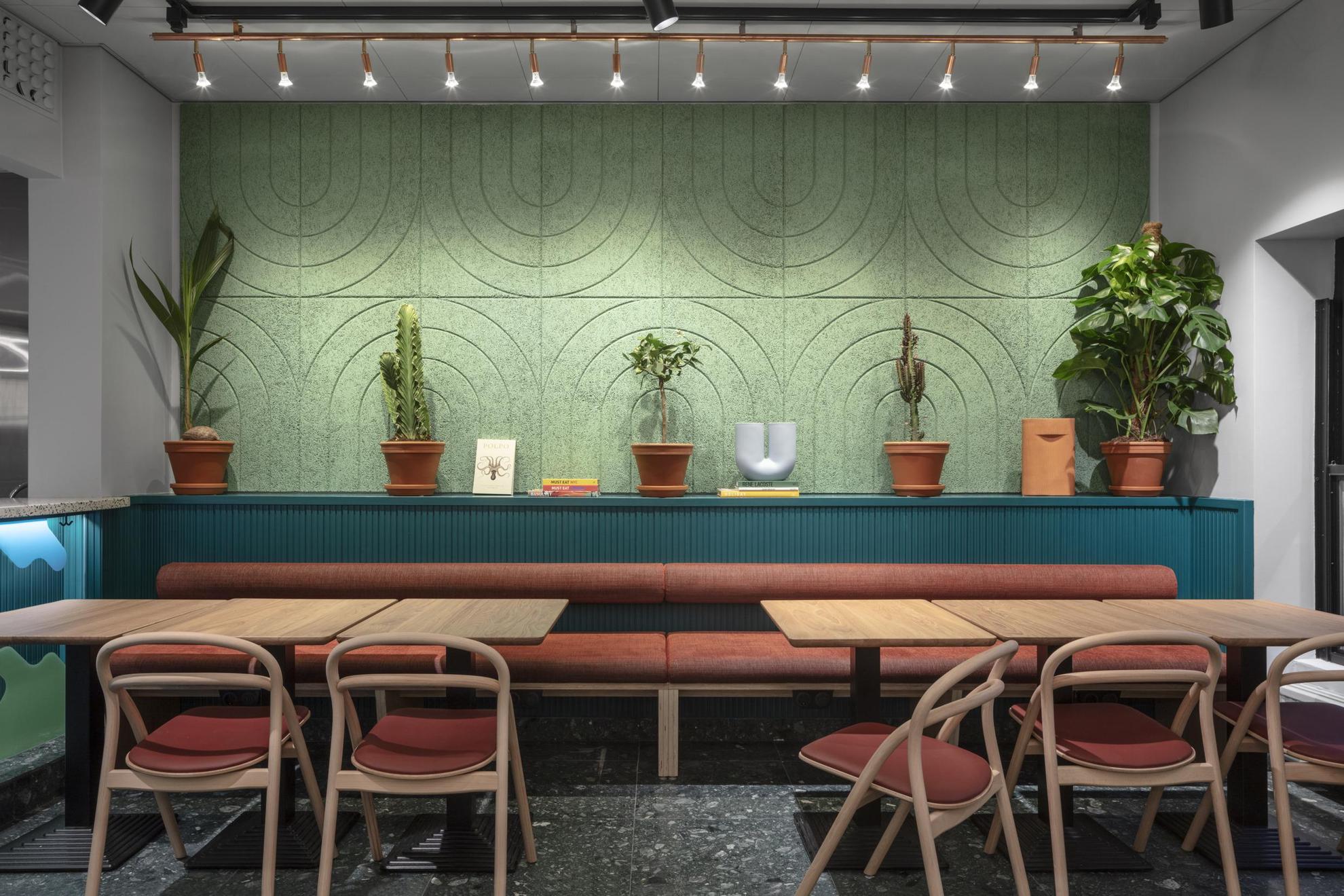 Ein Sitzbereich. Ein paar Pflanzen schmücken die grün-blaue Wand hinter dem Tisch.