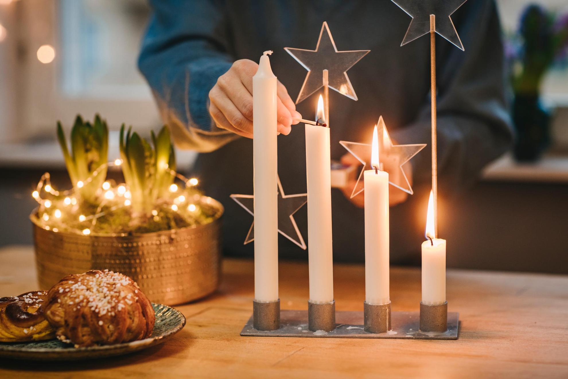 Eine Person zündet die Kerzen eines Adventsgestecks an.