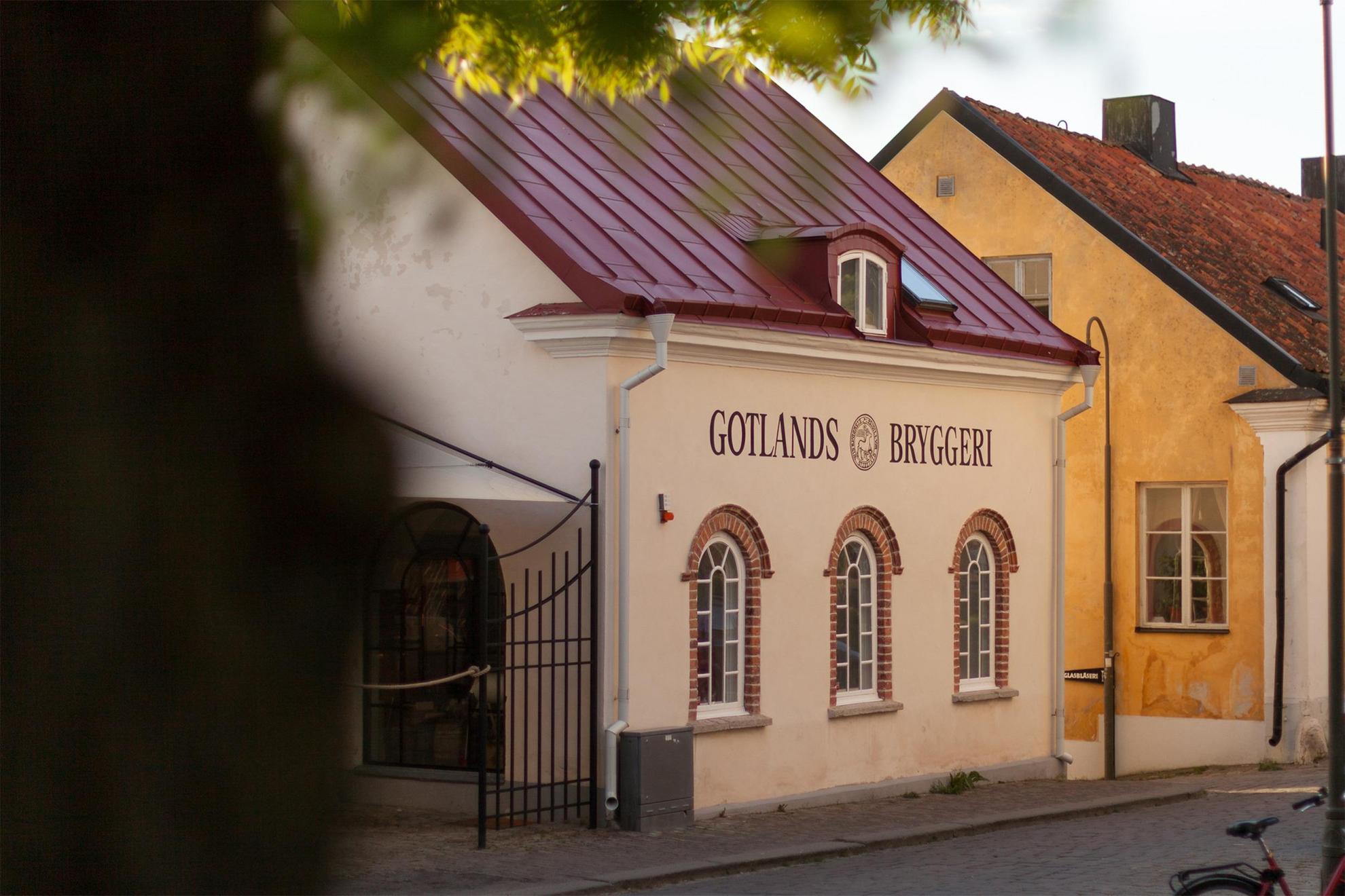 Eine Straße mit einem weißen Haus auf dem in dunkelroter Schridt Gotlands Bryggeri geschrieben steht.
