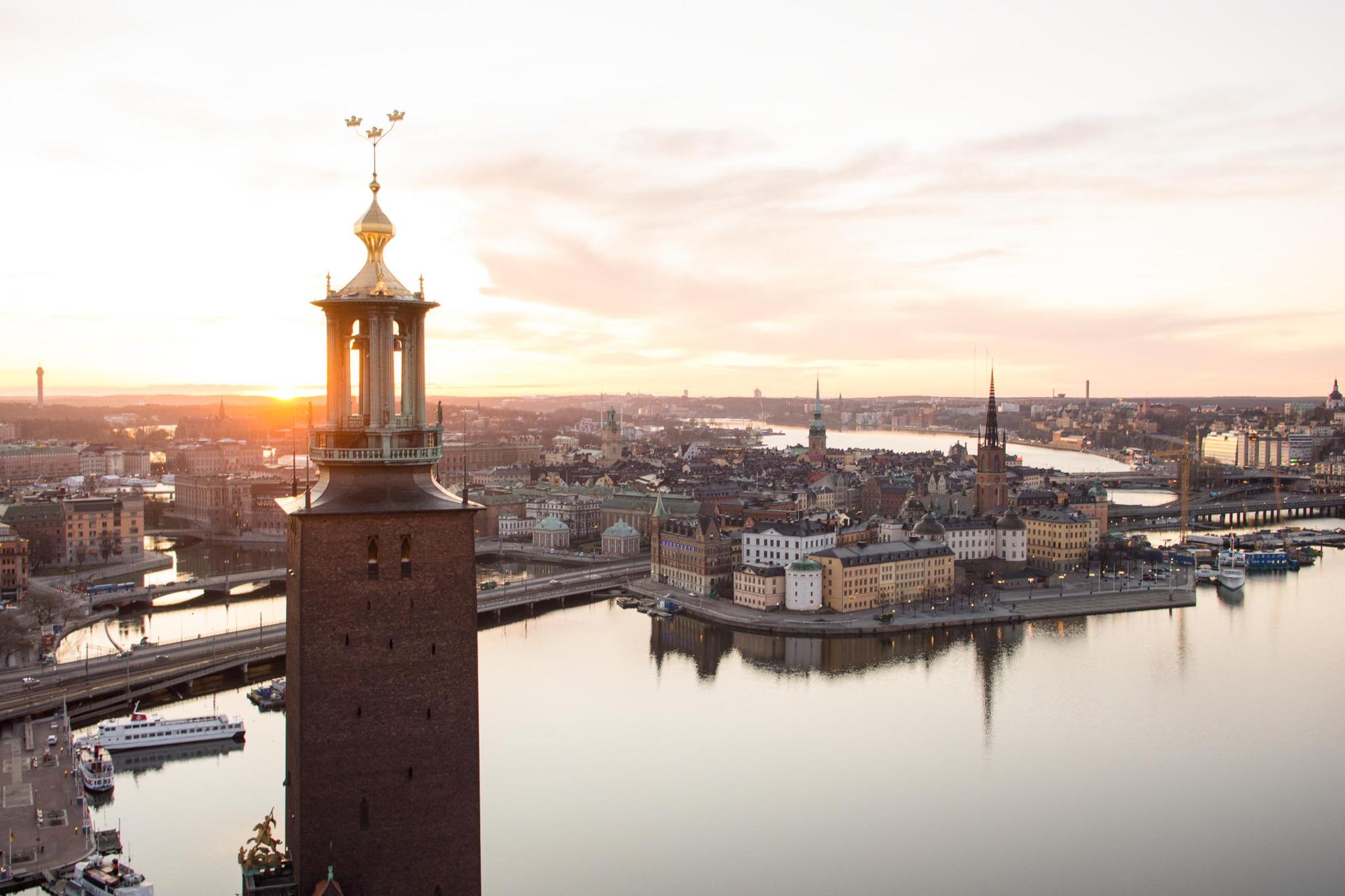 Die Skyline von Stockholm mit dem Mälarsee bei Sonnenuntergang und dem Rathausturm mit den drei Kronen im Vordergrund.