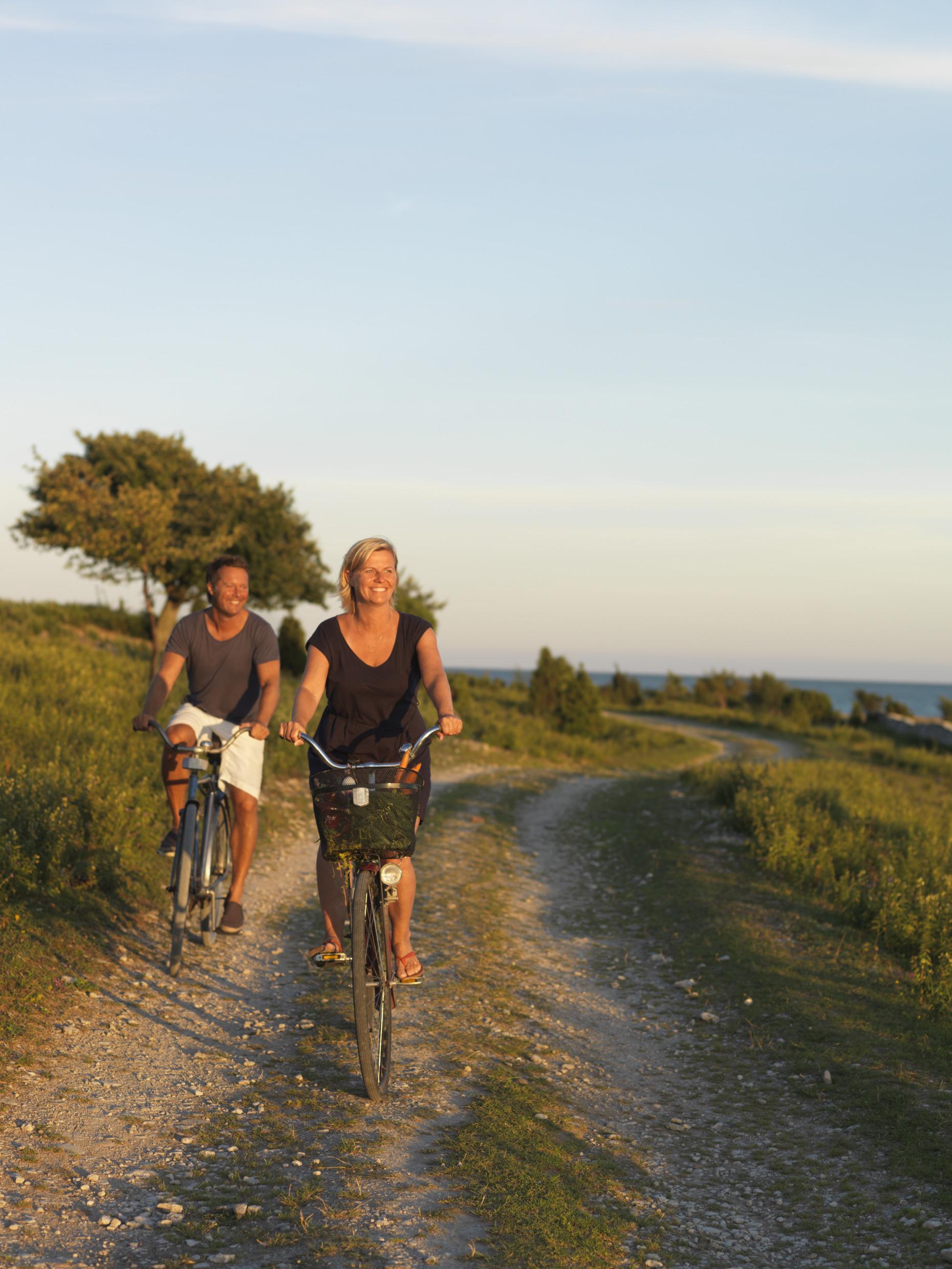 A woman and a man are biking on a gravel path along the coast of Fårö Island.
