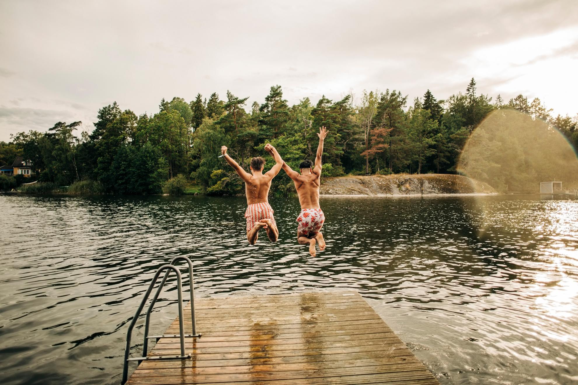Zwei Männer springen von einem Steg in einen See.