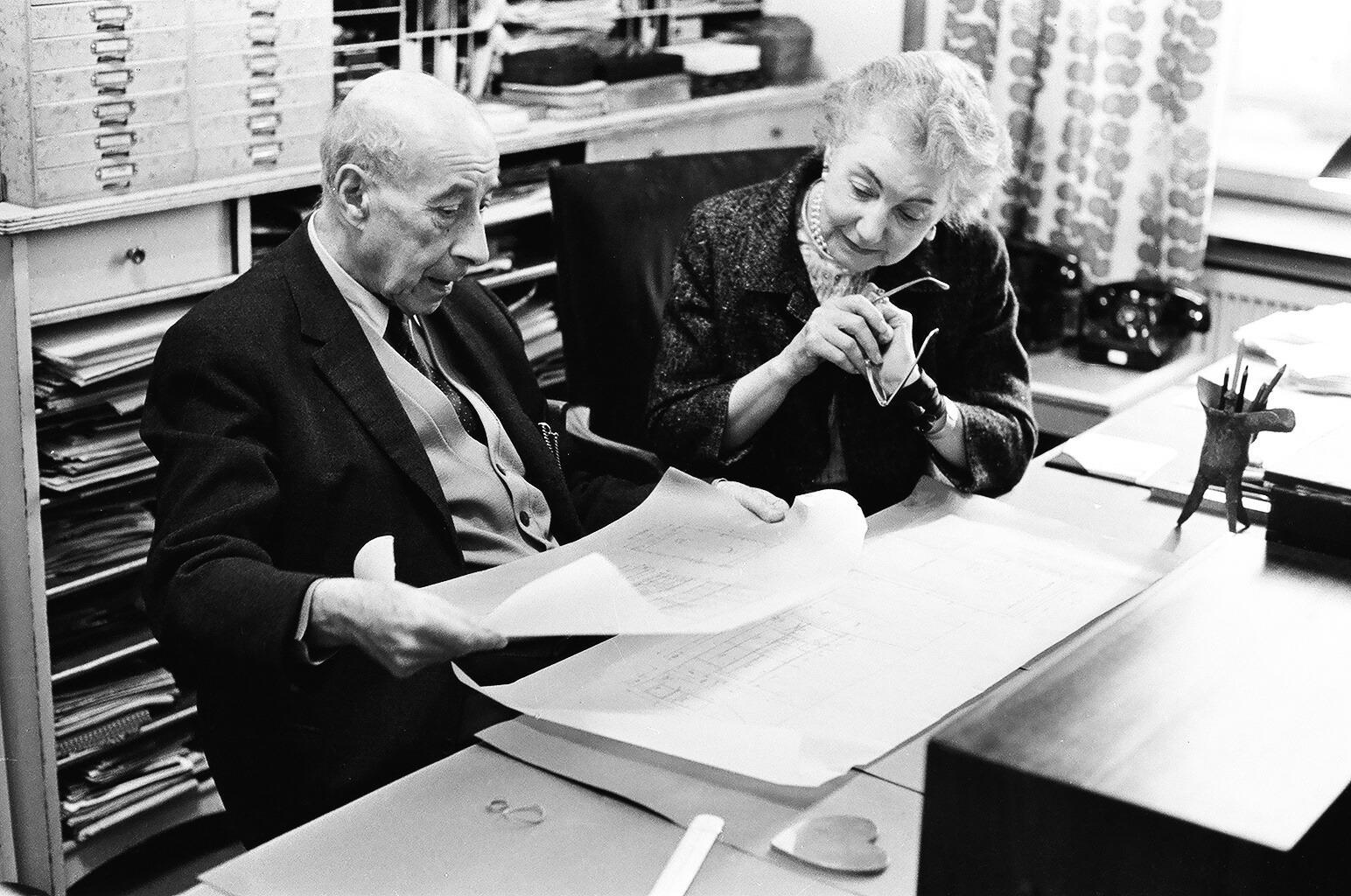 Josef Frank und Estrid Ericson sitzen an einem Schreibtisch und sehen sich Konstruktionszeichnungen an.