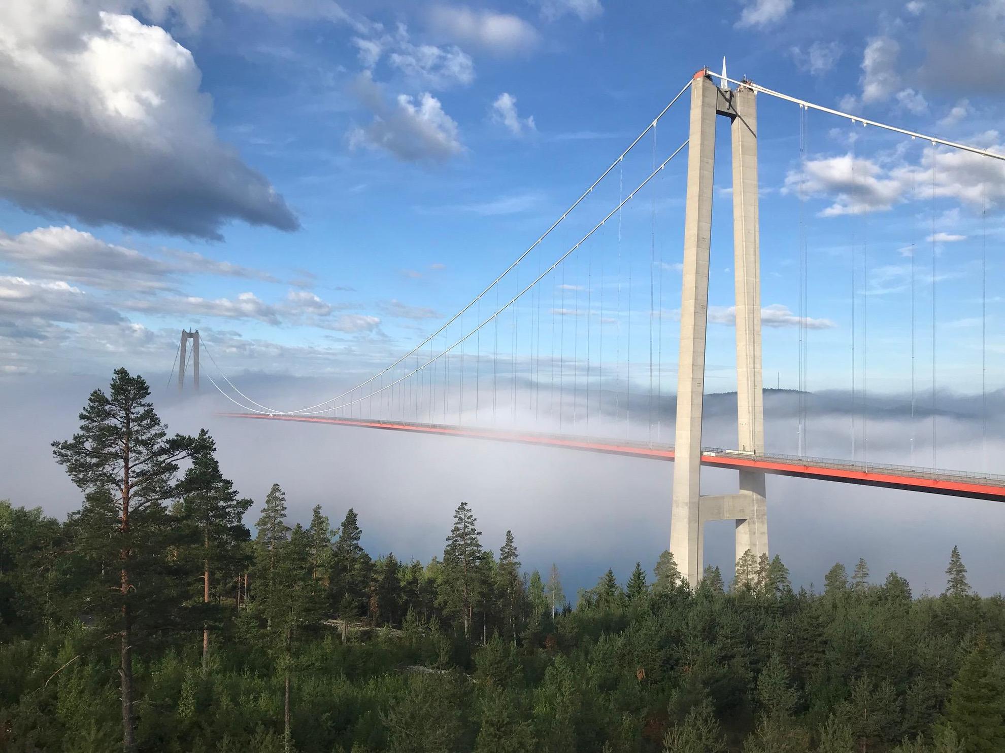 Eine lange Hängebrücke, die einen Fluss überquert, ist teilweise in Nebel gehüllt.