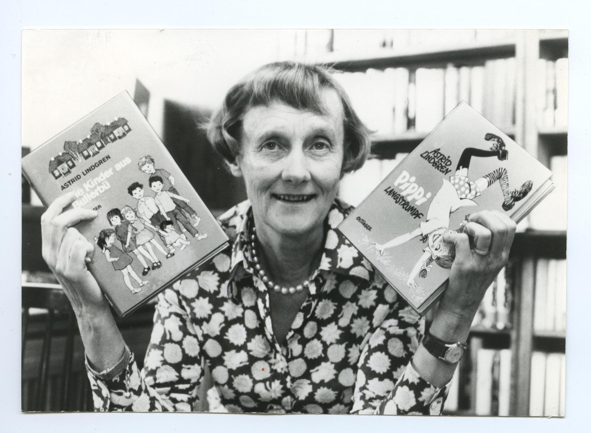 Ein Schwarz-Weiß-Porträt der Autorin Astrid Lindgren, die in der einen Hand ihr Buch Pippi Langstrumpf und in der anderen Hand das Buch Die Kinder des lärmenden Dorfes hält.