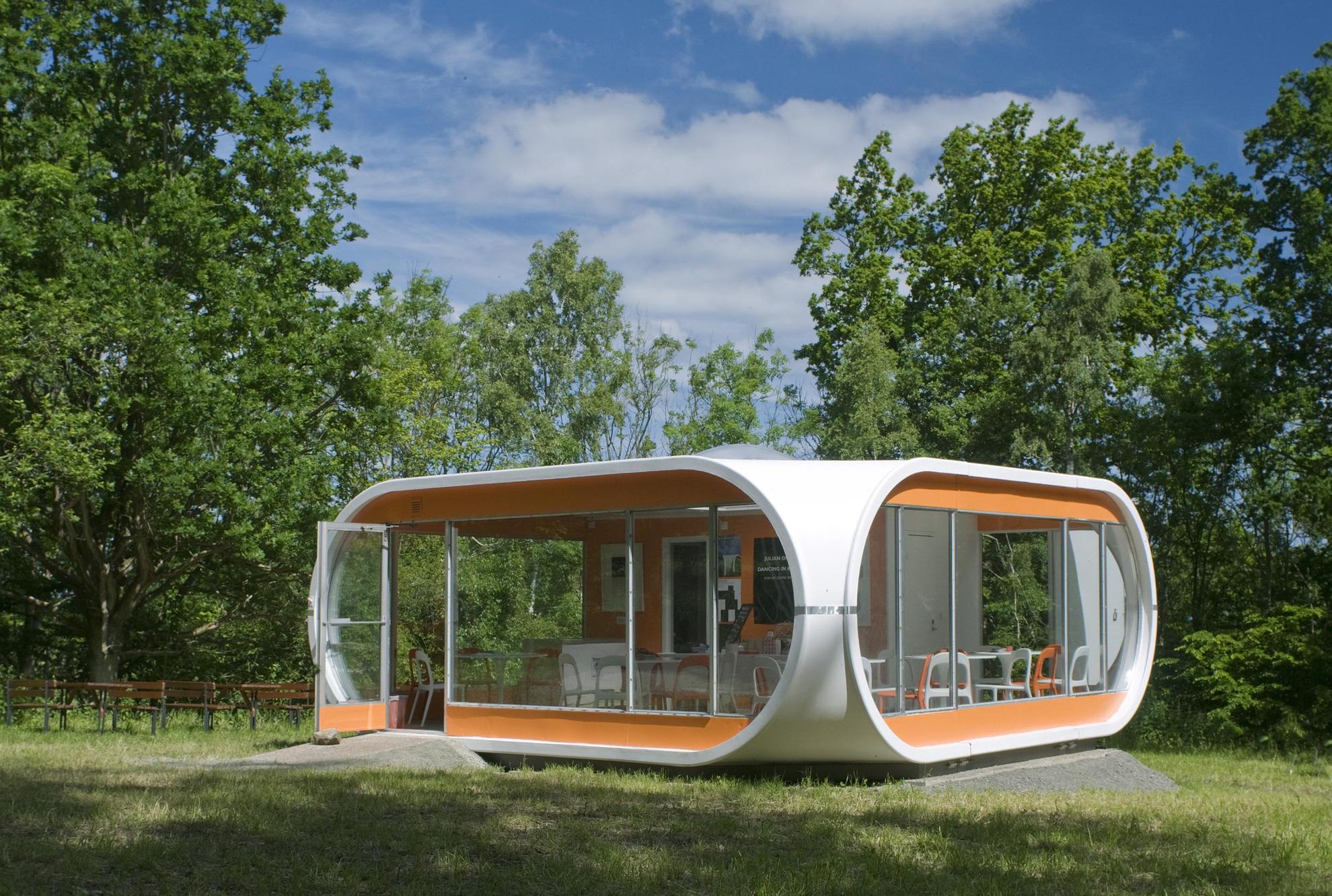 Kleines Häuschen aus orangefarbenem und weißem Kunststoff in einem Garten des Kivik Art Centre.