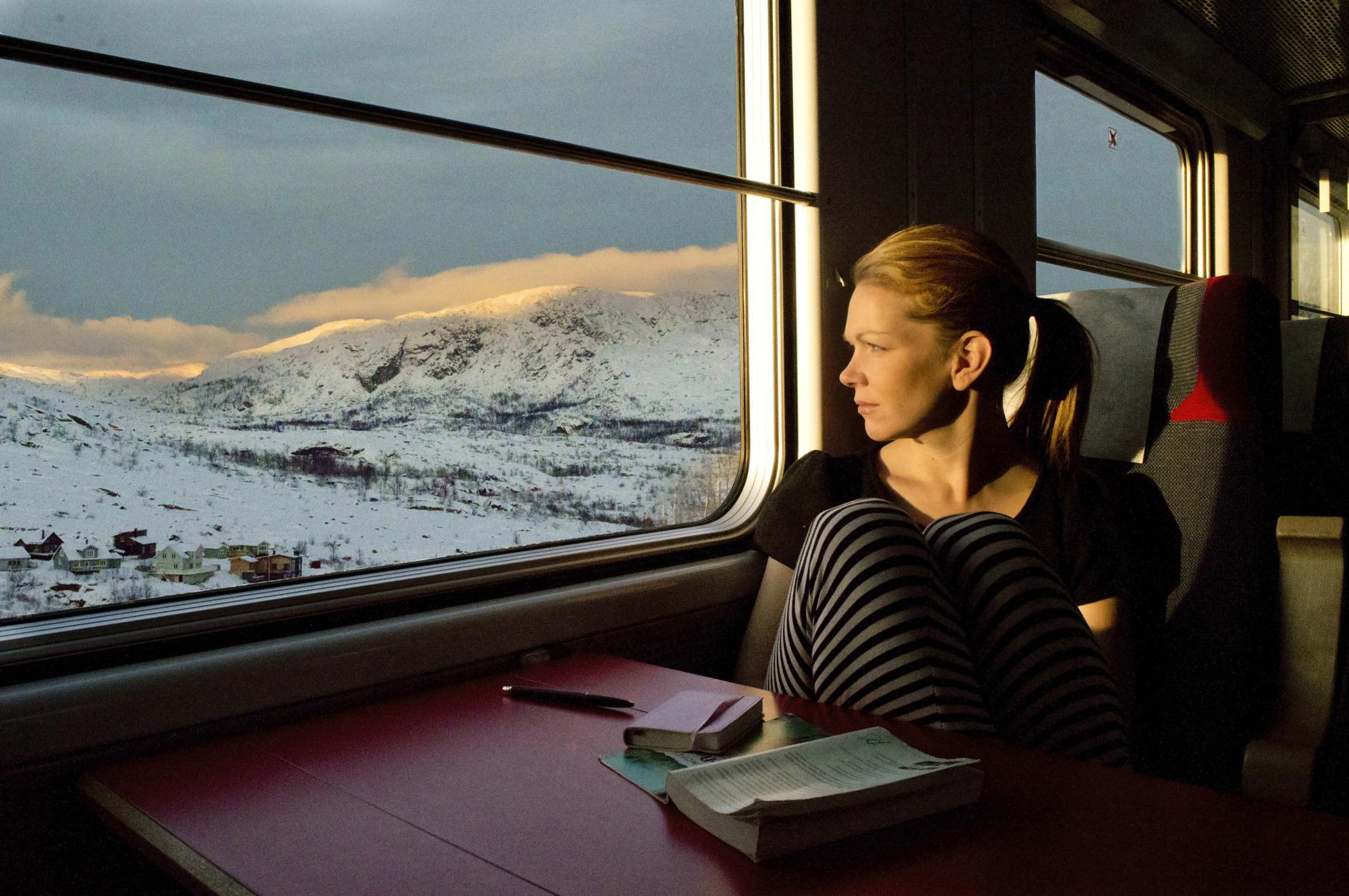 Eine Frau sitzt in einem Zug und blickt aus dem Fenster auf die Winterlandschaft draußen.