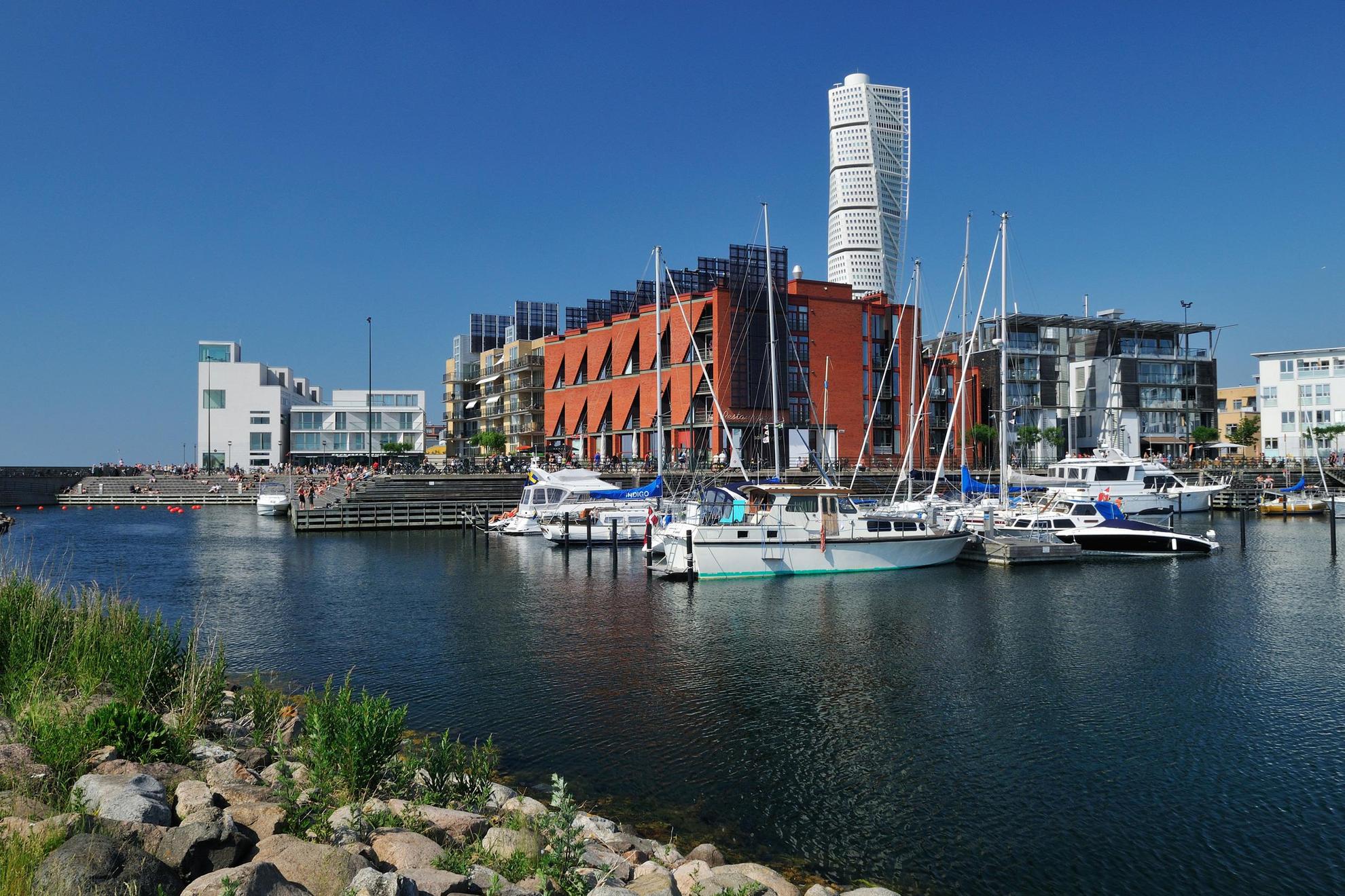 Private boats are moored next to apartment buildings in Malmö's Western Harbour district with the Turning Torso high-rise in the background.