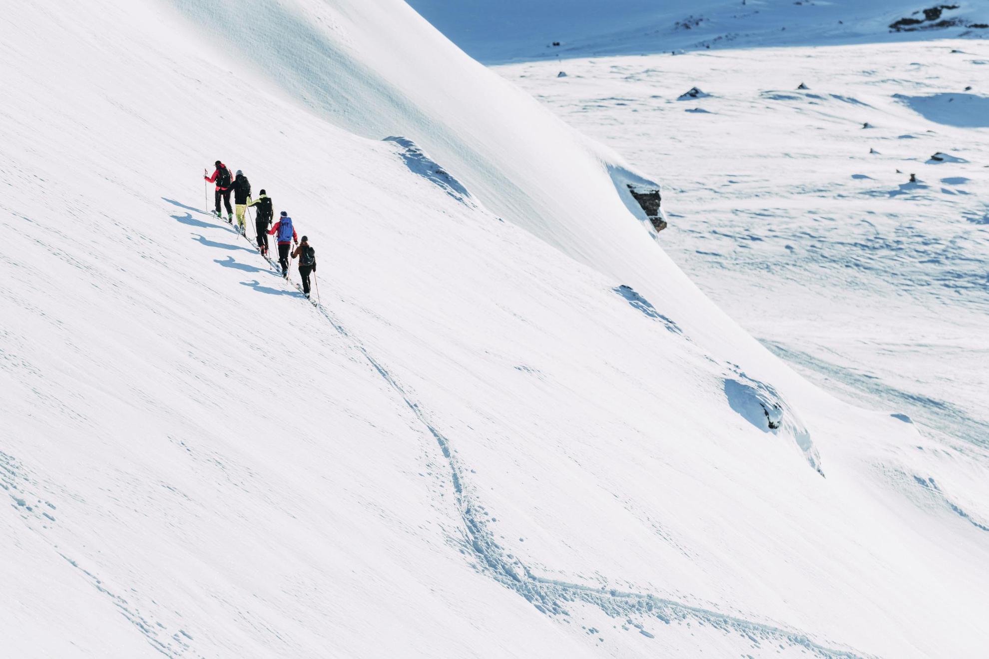 Fünf Personen mit Skiern sind auf dem Weg auf einen schneebedeckten Berg hinauf.
