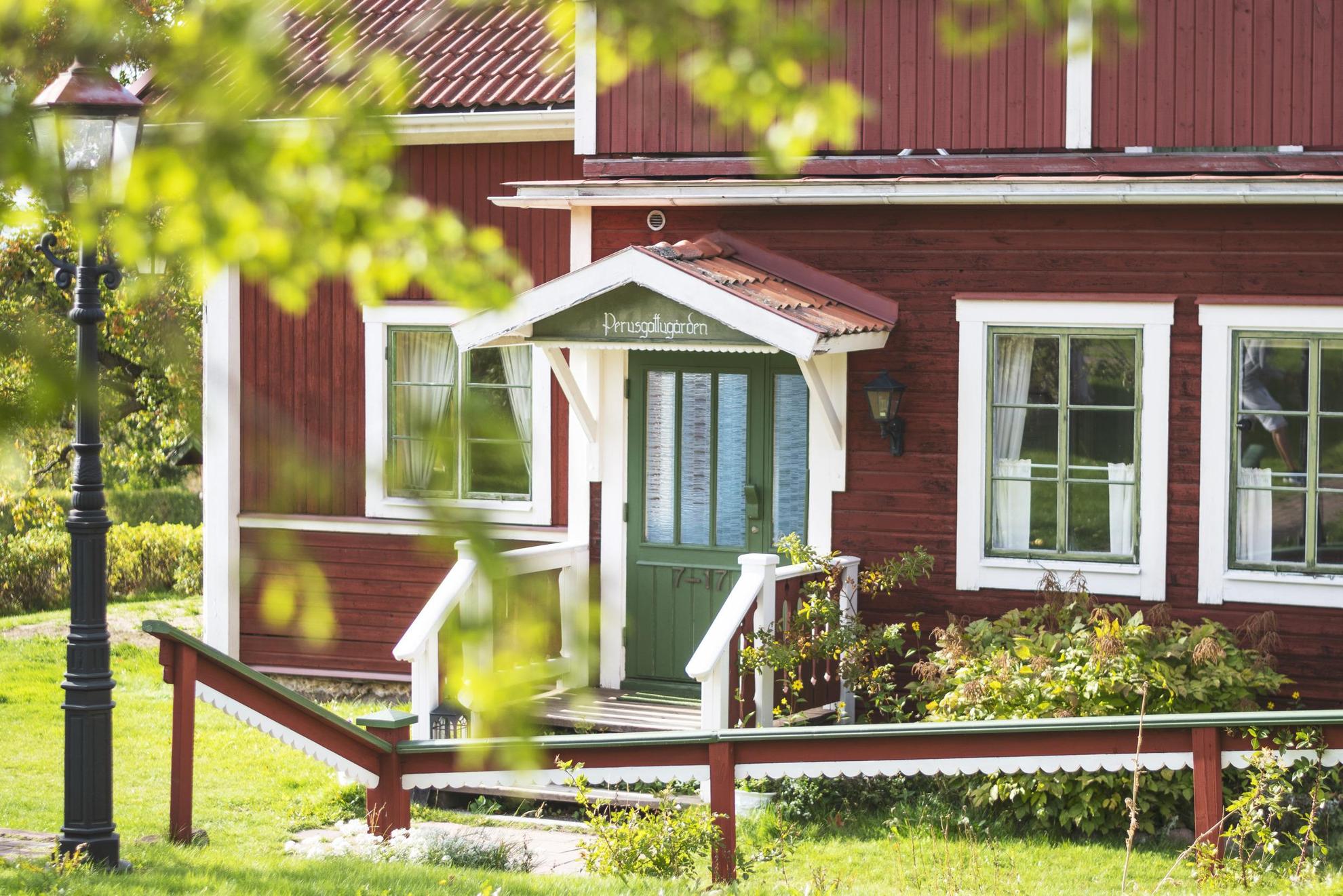 Ein rotes Holzhaus mit weißen Zierleisten und einer grünen Tür.